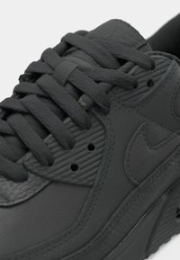 Gros plan sur une chaussure Nike noire montrant le cuir texturé, les lacets et le logo Nike swoosh sur le panneau latéral.