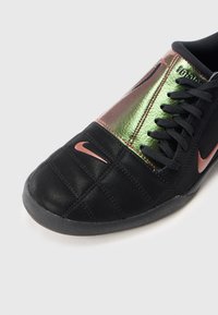 Czarno-metaliczne zielone buty sportowe Nike z logo w kolorze różowego złota, czarnymi sznurówkami i teksturowaną podeszwą na białym tle.