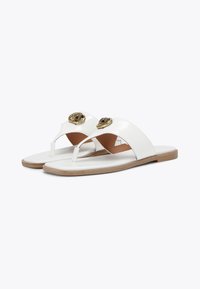 Sandali piatti bianchi con due accenti dorati sulla cintura superiore, caratterizzati da un design con post per le dita e una texture simile alla pelle liscia. Suola marrone.