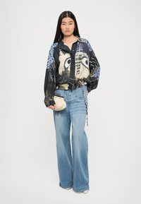 Loose black blouse with animal print accents, paired with light blue wide-leg jeans and a small cream handbag.
