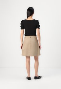 Top nero a maniche corte in tessuto texturizzato abbinato a una gonna beige a trapezio, in materiale liscio, lunghezza al ginocchio e dettagli di cucitura semplici.