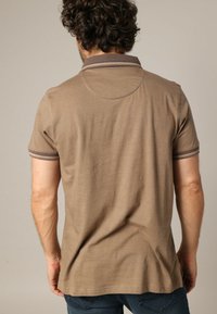 Polo marron avec col et poignets côtelés, manches courtes et design de tissu texturé. Vu de l'arrière, mettant en valeur le détail de l'encolure.