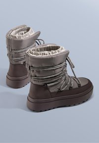 Szare wodoodporne buty z ściąganymi górami, wyposażone w szare sznurowadła i grubą brązową podeszwę. Wykonane z pikowanego nylonu o fakturowanej powierzchni.