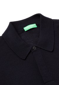 Camisa polo azul marino con un tejido texturizado, tapeta de dos botones y una etiqueta verde que dice "UNITED COLORS OF BENETTON" en el cuello.