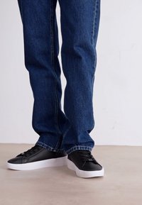Mörkblå denimjeans, rak passform, blekt utseende. Svarta snörskor med en vit gummisula och slät ovandel.