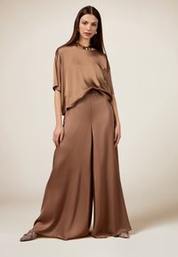 Haut en satin marron à coupe ample, associé à un pantalon large assorti avec une fente à l'avant, complété par des chaussures à bout pointu.