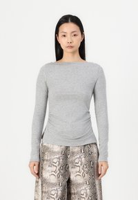 Grijze langemouwen top met een bootnek en gatherdetails aan de zijkanten, gecombineerd met losse, textuurachtige slangenprint broeken.