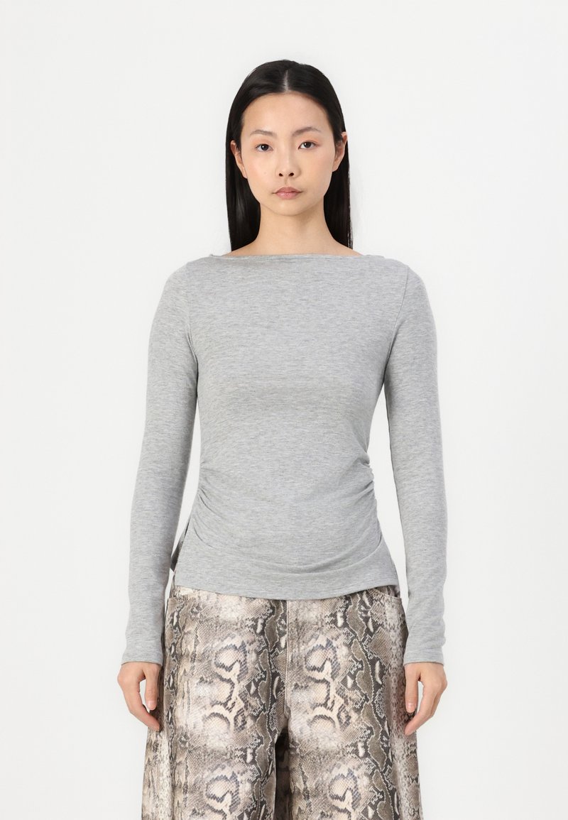 Gray long-sleeve top with a boat neckline and gathered side details, paired with loose-fitting, textured snake print pants.