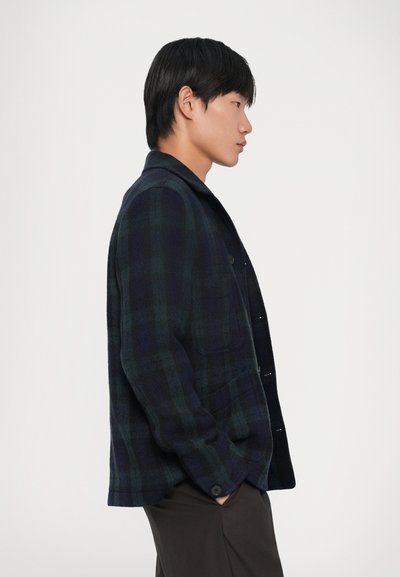 Giacca a plaid blu navy e verde, realizzata in tessuto morbido. Presenta una vestibilità comoda, chiusura con bottoni e una tasca frontale, con colletto standard.