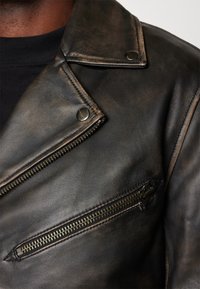 Zwarte leren motorjack met een verweerd uiterlijk, opvallende revers, twee ritszakken en metalen hardware accenten.