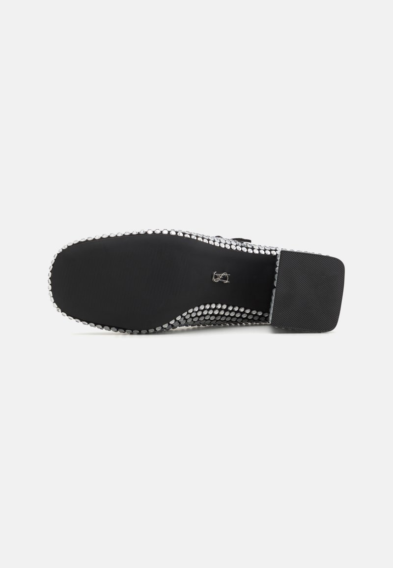 Scarpa piatta con una suola nera liscia, circondata da borchie circolari argentate lungo il bordo. Il design è semplice con un tacco quadrato.