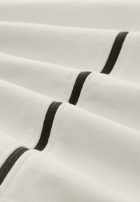 Textile blanc avec un motif texturé, présentant des rayures noires horizontales à intervalles réguliers, créant un design contrasté.
