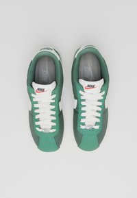 Zelene i sive tenisice s bijelim vezicama, Nike logo na jeziku i strani, teksturirani materijal, dizajn s okruglim vrhom i gumenom potplatom.