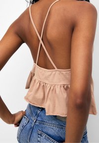 Cropped top beige chiaro con bordo svasato, dotato di spalline incrociate sul retro e una finitura morbida e texturizzata. Indossato con pantaloni shorts in denim blu.