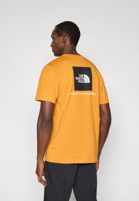 Κοντομάνικο T-shirt σε μουσταρδί κίτρινο χρώμα από βαμβάκι. Διαθέτει μαύρο τετράγωνο λογότυπο με το κείμενο "THE NORTH FACE" και "NEVER STOP EXPLORING" στην πλάτη.