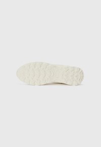 Sneaker sole in off-white rubber with a textured tread pattern; features angled lugs for traction and a smooth central area for flexibility.