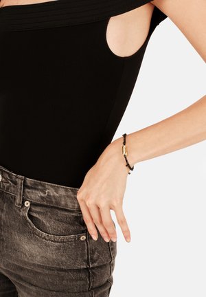 Pulsera de cuentas negras con un detalle dorado, llevada en la muñeca, combinada con un body negro y unos vaqueros grises de tiro alto.