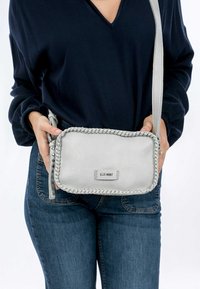 Borsa a tracolla in pelle grigia con bordi intrecciati, forma rettangolare, chiusura con zip e piccola placca con logo sul davanti. Texture liscia.