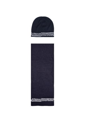 Ensemble bonnet et écharpe en tricot navy avec un logo "ARMANI EXCHANGE" blanc contrastant sur le revers des deux pièces. Texture douce, design simple.