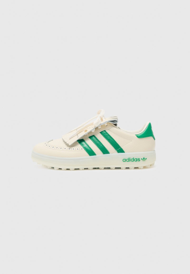 Baltas ādas sneakers ar zaļām svītrām, apaļu purngalu un teksturētām akcentiem. Iekļauj plakanu šņoru aizdares sistēmu un "adidas" logo zaļā krāsā.