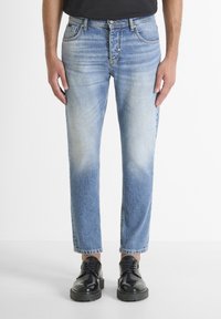 Jeans de mezclilla azul claro con un diseño deslavado, corte recto, estilo de cinco bolsillos y cierre de botón, combinados con zapatos de cuero negros.