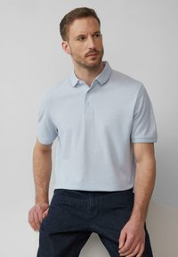 Hellblaues Poloshirt aus Baumwolle mit Kragen, kurzen Ärmeln und einer Knopfleiste mit drei Knöpfen sowie einer glatten, strukturierten Oberfläche.
