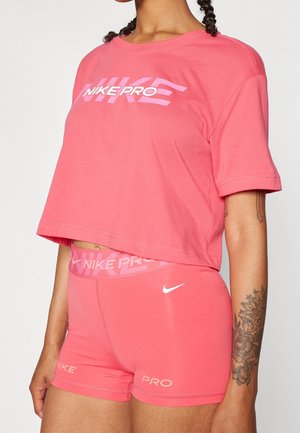 Vrouw draagt roze Nike Pro trainingsshorts en een bijpassend cropped T-shirt met Nike Pro-logo's, met een bloemtattoo op haar arm.