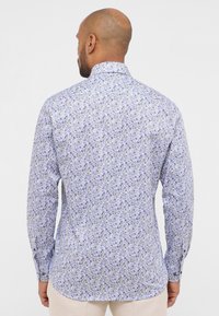 Camicia a maniche lunghe di colore azzurro chiaro con stampa floreale. Presenta un colletto button-down e una vestibilità su misura, con polsini a bottoni e orlo curvo.