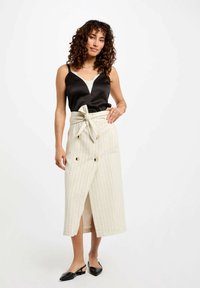 Camisón de satén negro con encaje en el dobladillo, combinado con una falda envolvente a rayas beige que cuenta con un cinturón atado y acentos de botones dorados.