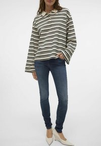 Svītraina garenā piedurkņu polo krekls krēmkrāsā, melnā un pelēkā, ar apkakli. Apvienots ar ziliem ādas biksēm un baltām norādītām kurpēm.