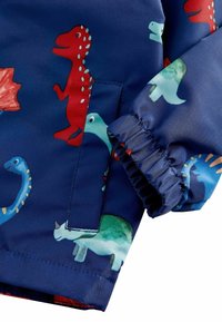 Veste de pluie bleue pour enfants ornée de divers motifs de dinosaures en rouge et vert, avec des poignets élastiques, une poche frontale et une texture lisse.
