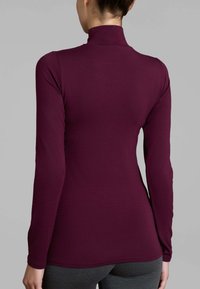 Top lungo bordeaux con collo a imbuto, design aderente e texture liscia. Il tessuto è elasticizzato e senza cuciture all'orlo e ai polsini.