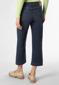 Dark blue cropped jeans with a straight leg, featuring a classic five-pocket design and contrasting stitching. Beige slip-on shoes complete the look.