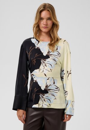 Femme portant un haut à manches longues avec un grand imprimé floral bleu clair partagé entre des sections de tissu noir et crème.