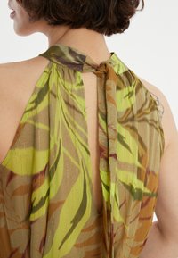 Top sans manches vert et marron avec un motif floral, présentant un dos en trou de serrure et un col noué. Tissu léger et texturé.