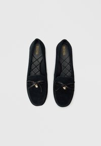 Μαύρες moccasin παντόφλες από σουέντ με επένδυση καπιτονέ, επίπεδες σόλες και διακοσμητικό φιόγκο από κορδέλα. Διαθέτουν μικρό χρυσό διακοσμητικό στοιχείο.