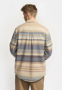 Multigestreepte flanellen shirt in beige, blauw en roest. Heeft een afgeronde zoom en rugpand, met lange mouwen en een knoopsluiting bij de kraag.