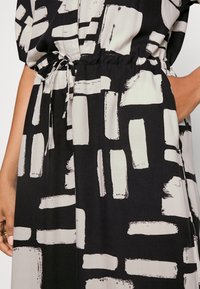 Vestido de estampado en blanco y negro con un diseño holgado, cintura elástica y detalle de lazo. La tela tiene una textura suave y lisa.