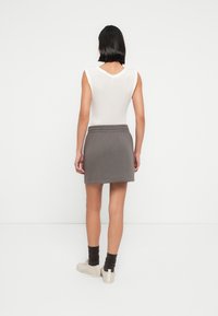 Γκρι βαμβακερή φούστα με ελαστική μέση, συνδυασμένη με λευκό αμάνικο τοπ. Το μοντέλο φοράει μπεζ αθλητικά παπούτσια και σκουρόχρωμες καφέ κάλτσες.