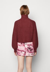 Dikke wijnrode gebreide trui met een hoge kraag, gecombineerd met een geprinte roze minirok met abstracte patronen en tekstontwerpen.