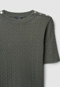 Pull en tricot vert avec un motif de câbles texturé, manches courtes et boutons pression métalliques sur l'épaule gauche.