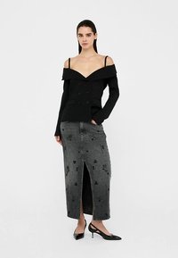 Mustast õlgadeta jakk kahekordsete nuppudega, mida täiendab pikk hall teksaseelik lillekaunistuste ja eeslõhikuga.