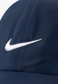 Navy blue cap made of smooth fabric featuring a white embroidered logo on the front, with visible stitching and a structured design.