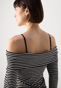 Haut à rayures noir et blanc, décolleté bardot avec des manches longues, doté de bretelles réglables noires et d'une coupe ajustée. Texture lisse.