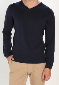 Pull col en V bleu marine en maille douce. Manches longues, poignets et ourlet côtelés, coupe ajustée, avec une texture lisse.