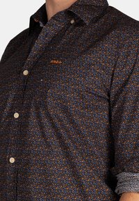 Kortarmig blouse in donkere stof met een bladerenpatroon in blauw en oranje. Bevat een klassieke kraag en beige knopen.