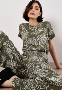 Completo di top e pantaloni verde oliva con motivi floreali bianchi. Tessuto leggero, con una vestibilità comoda e vita elastica. Calzature nere semplici.