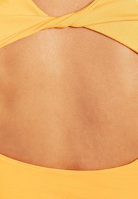 Gelbes Stoffoberteil mit einem Twist-Design auf der Rückseite, das einen offenen Rückeneinsatz bietet. Glatte Textur mit taillierter Form.