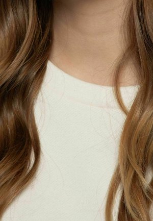 Cheveux longs, ondulés et châtain clair tombant sur un haut blanc à col rond, laissant voir le cou et le haut de la poitrine sans visage visible.