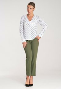 Biała bluzka w mały kwiatowy wzór, dekolt w serek, z zapięciem na guziki. Oliwkowe dopasowane spodnie, slim fit, noszone z czarnymi szpilkami.